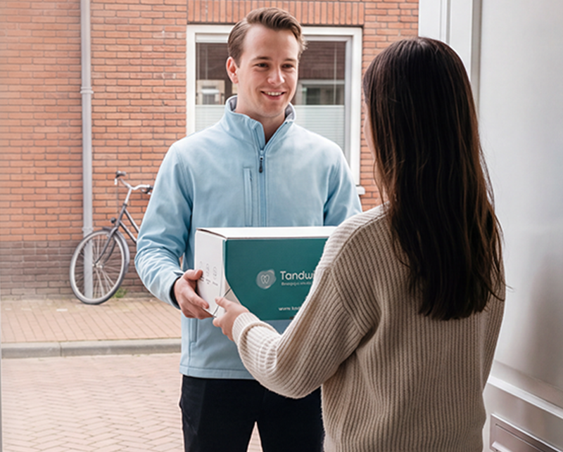 Bezorger overhandigt Tandwinkel-doos aan klant voor de voordeur