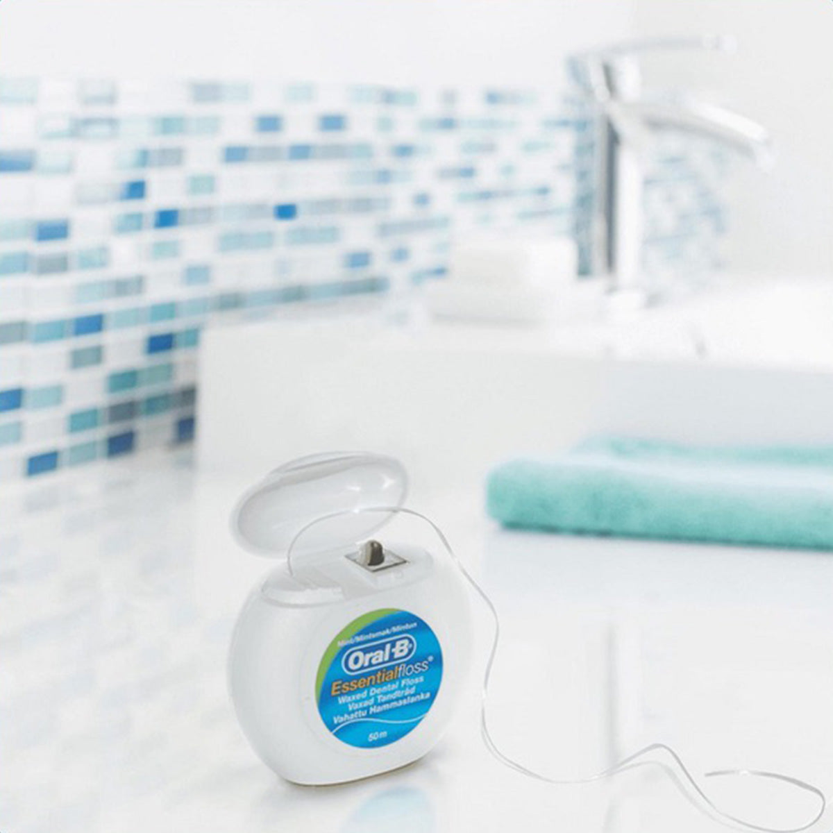 Oral-B Essential Floss waxed doosje open op badkamerrand met tegels op achtergrond