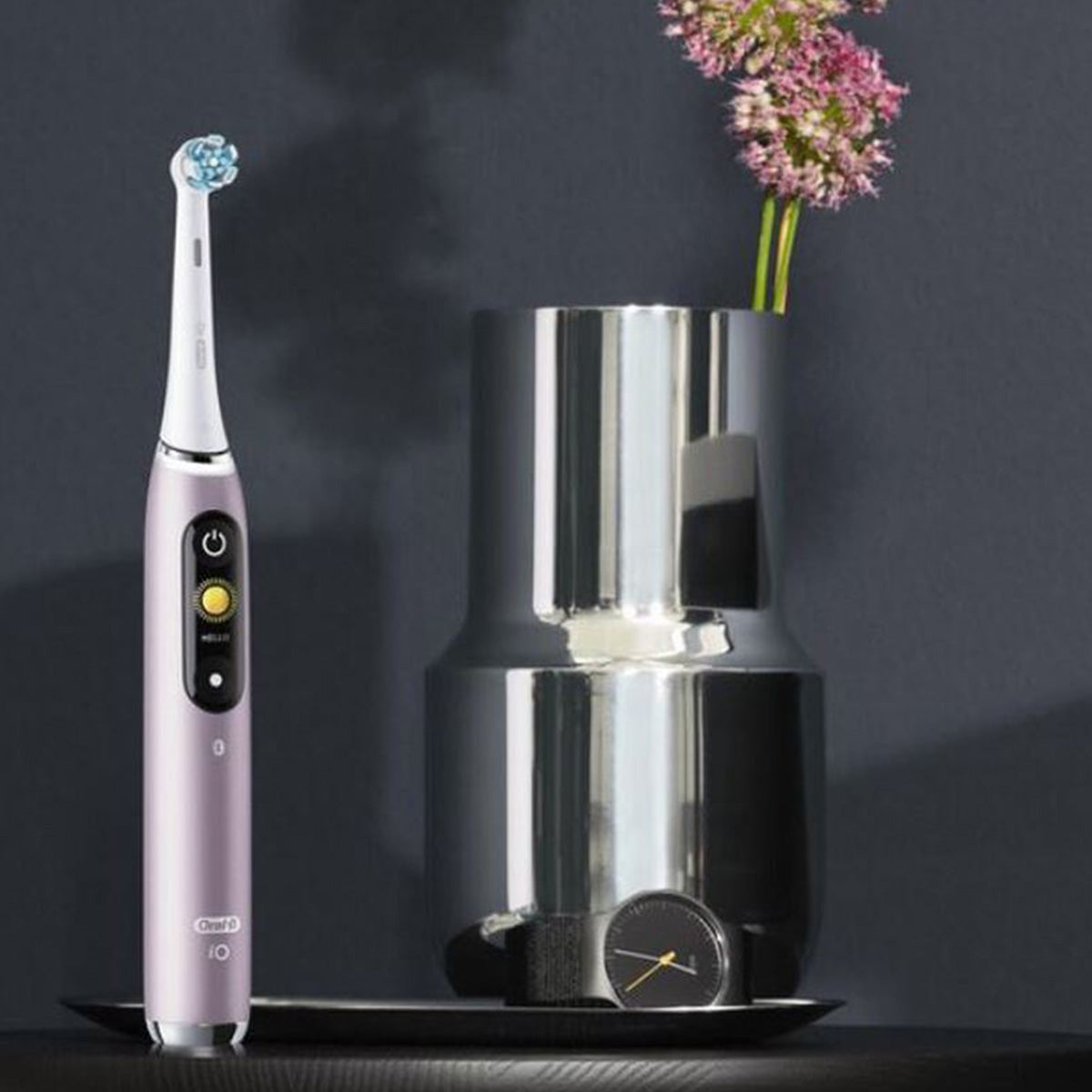 Oral-B iO 9 Roze Quartz tandenborstel op dienblad naast zilveren vaas met bloemen