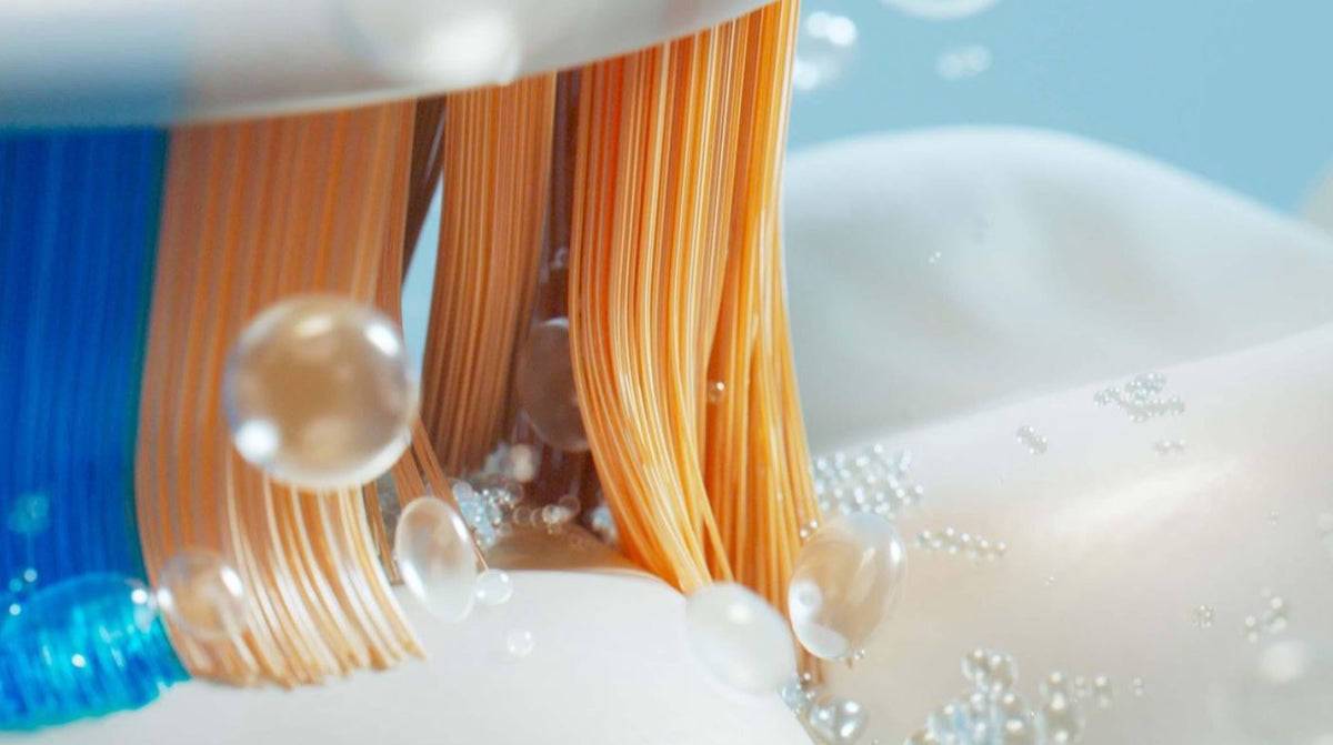 Sonicare A3 Premium AIO opzetborstel close-up met blauwe en oranje haren en waterdruppels