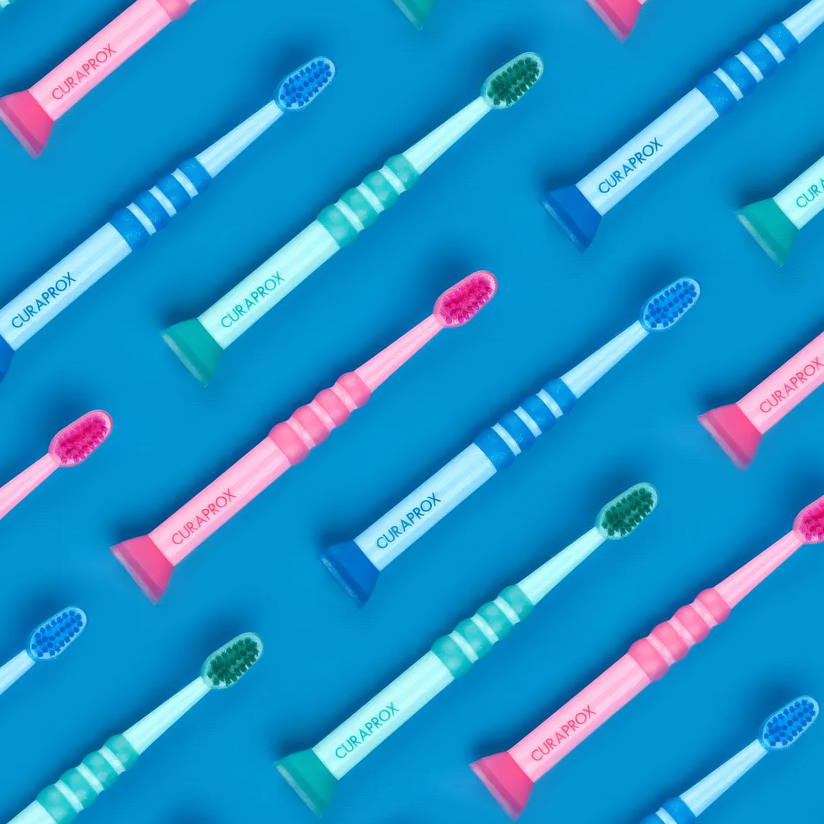 Curaprox Tandenborstel Baby in roze, blauw en groen op rij op blauwe achtergrond