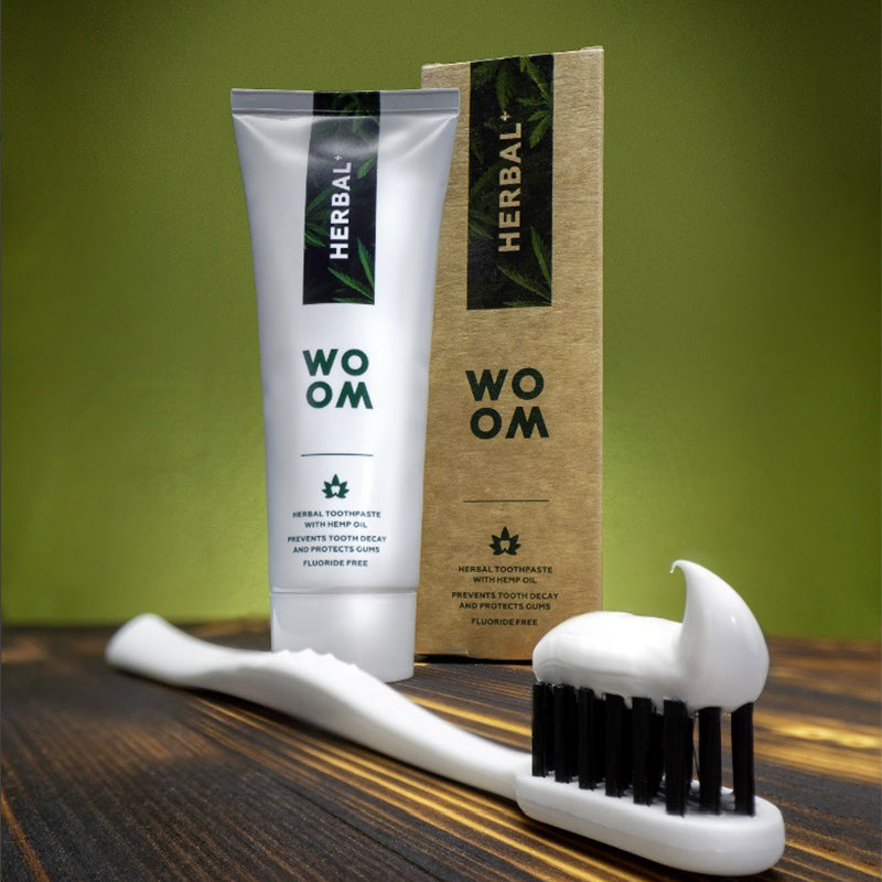 Woom tandpasta Herbal+ op tandenborstel met zwarte haren en verpakking op houten ondergrond