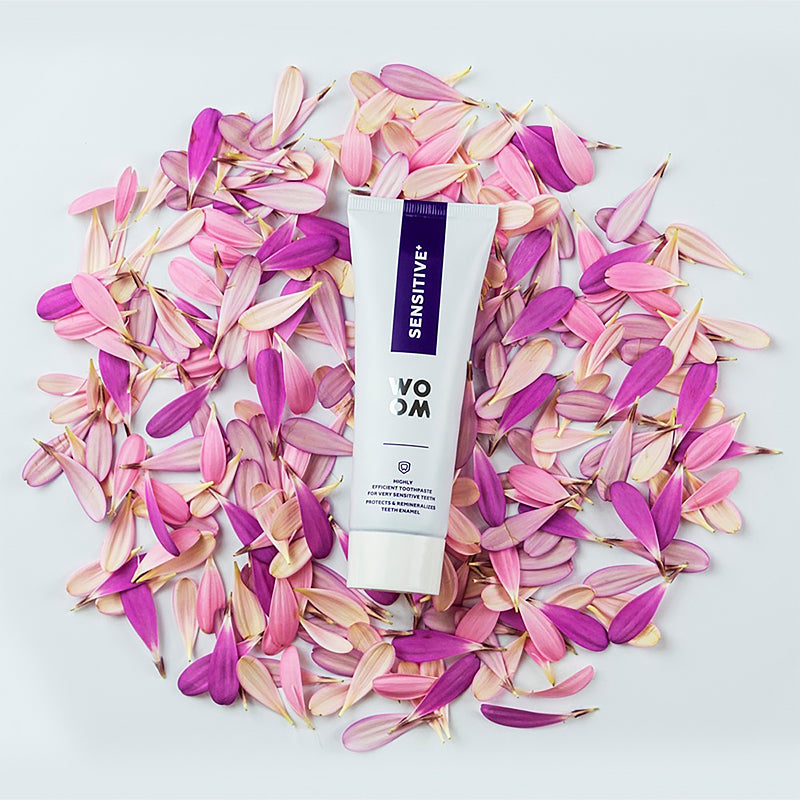 Woom tandpasta Sensitive+ tube liggend op roze en paarse bloemblaadjes