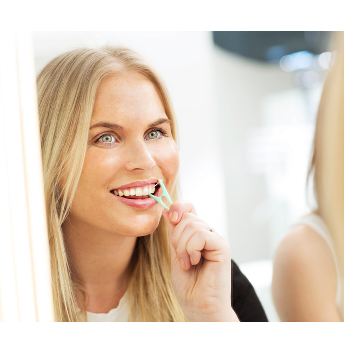 Jordan Easy Reach Flosser gebruikt door lachende vrouw voor de spiegel