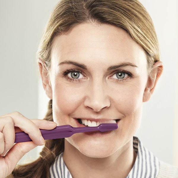 Vrouw poetst tanden met paarse TePe Select X-soft tandenborstel