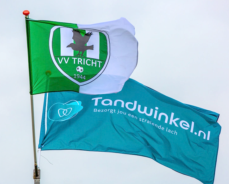 Vlaggen van VV Tricht en Tandwinkel.nl wapperen naast elkaar in de lucht