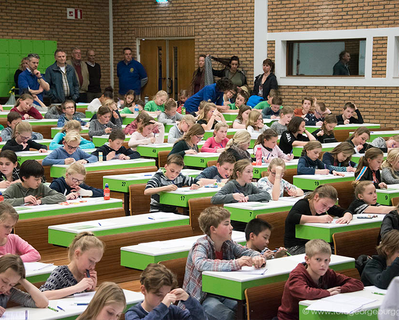 Kinderen maken een toets in collegezaal met groene banken