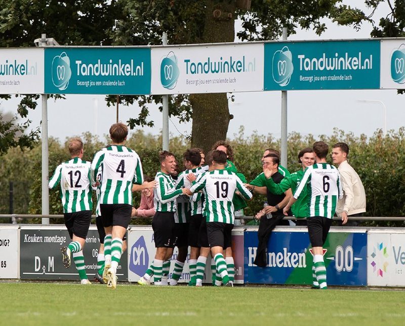 Voetbalteam in groen-wit tenue viert doelpunt bij Tandwinkel.nl reclameborden